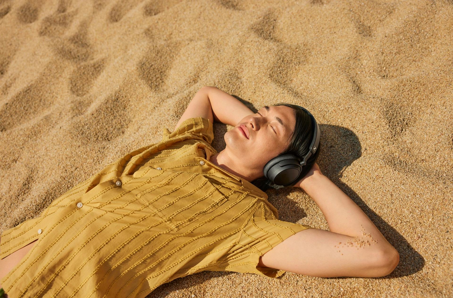 Vrouw ligt in zand met koptelefoon van Sennheiser